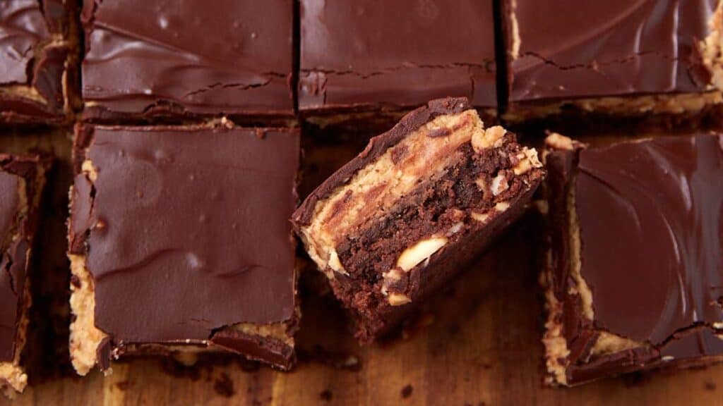 Close-up of chocolate peanut butter bars cut into squares. One bar is turned on its side, showing chocolate, peanut butter, and peanuts—holiday dessert bars that beat cookies for both flavor and festive flair.