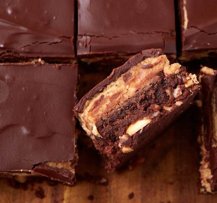 Close-up of chocolate peanut butter bars cut into squares. One bar is turned on its side, showing chocolate, peanut butter, and peanuts—holiday dessert bars that beat cookies for both flavor and festive flair.