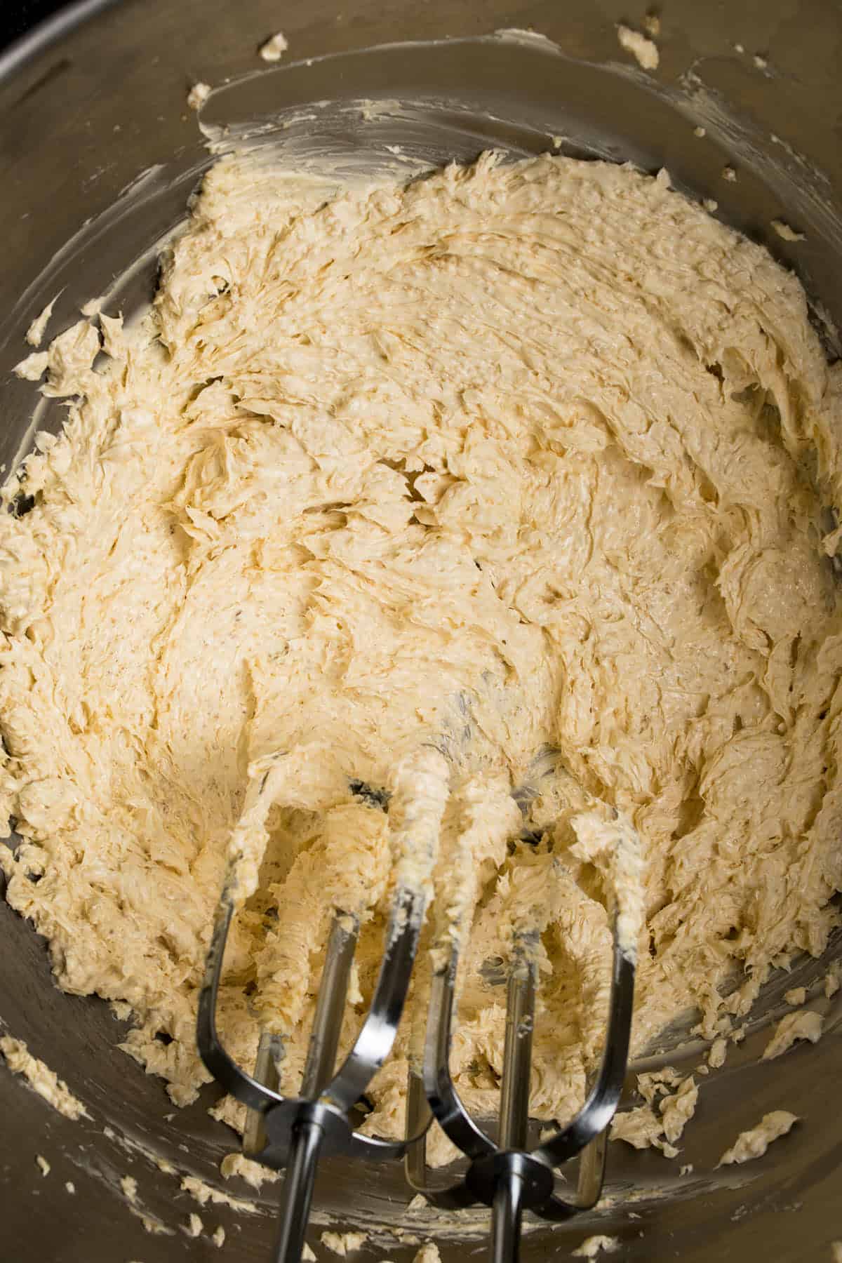 Close-up of a metal mixing bowl filled with creamy, pale yellow batter for Dutch Oven Bread. Two electric hand mixer beaters, coated in the mixture, rest in the bowl. The batter appears smooth and fluffy.