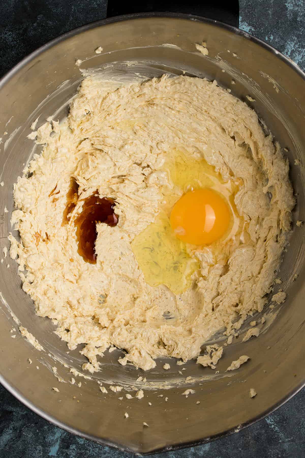 A metal mixing bowl with creamed butter and sugar, an egg, and a splash of vanilla extract, ready to be mixed together—a perfect start before serving alongside freshly baked Dutch Oven Bread.