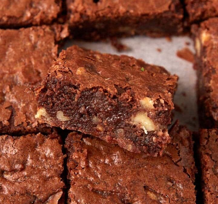 A batch of chocolate brownies cut into squares, with one brownie placed at an angle on top of the others to show its fudgy texture and chocolate chips inside.