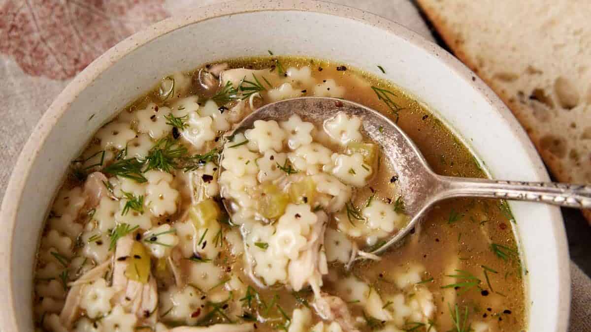 A bowl of orzo chicken soup with lemon slices next to it. 