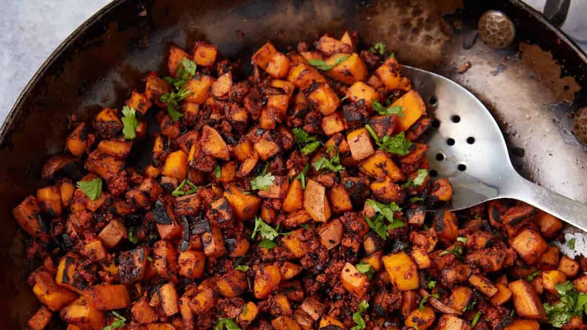 A skillet filled with sautéed diced potatoes, chorizo, and sweet potato hash, garnished with chopped