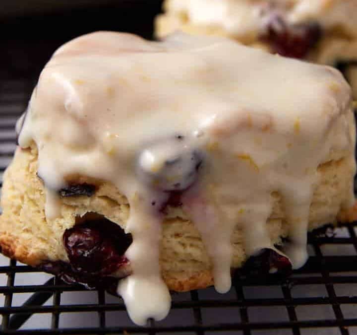 A freshly baked scone with cherries and white glaze sits on a cooling rack—one of those Easter brunch favorites families make year after year, with more scones and a baking tray blurred in the background.