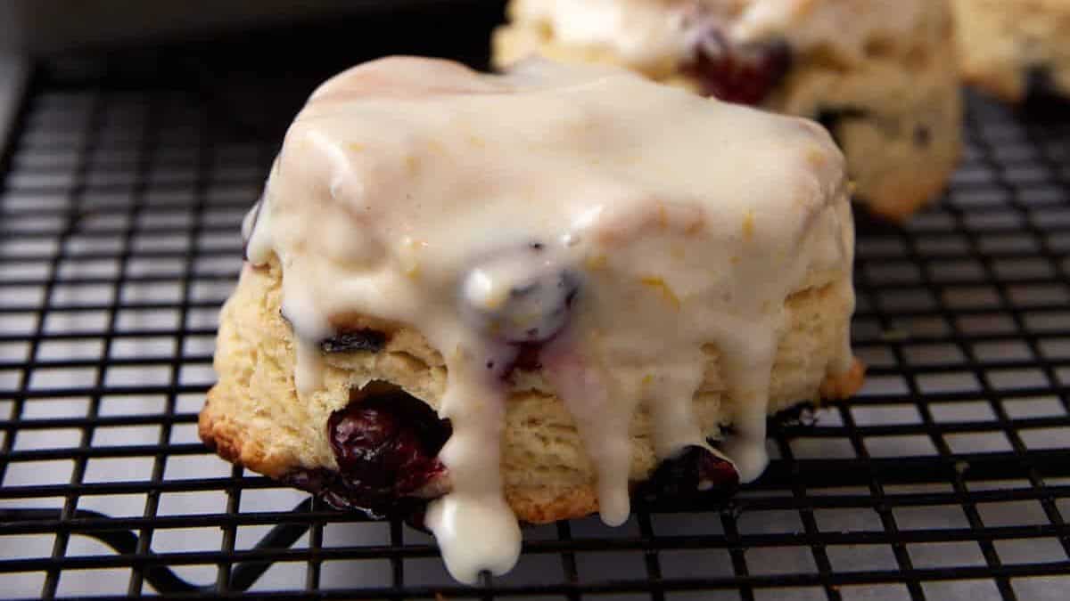 A freshly baked scone with cherries and white glaze sits on a cooling rack—one of those Easter brunch favorites families make year after year, with more scones and a baking tray blurred in the background.
