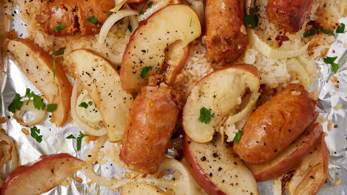 Sausage sheet pan dinner featuring sliced sausages, apple wedges, and onions baked on a foil-lined 