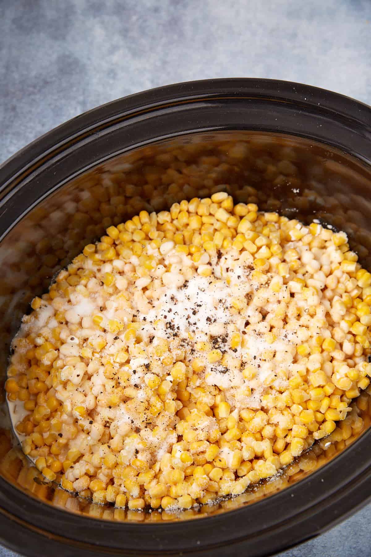 Slow cooker creamed corn features corn kernels topped with a creamy blend of milk, black pepper, and seasonings, all ready to be cooked to perfection.
