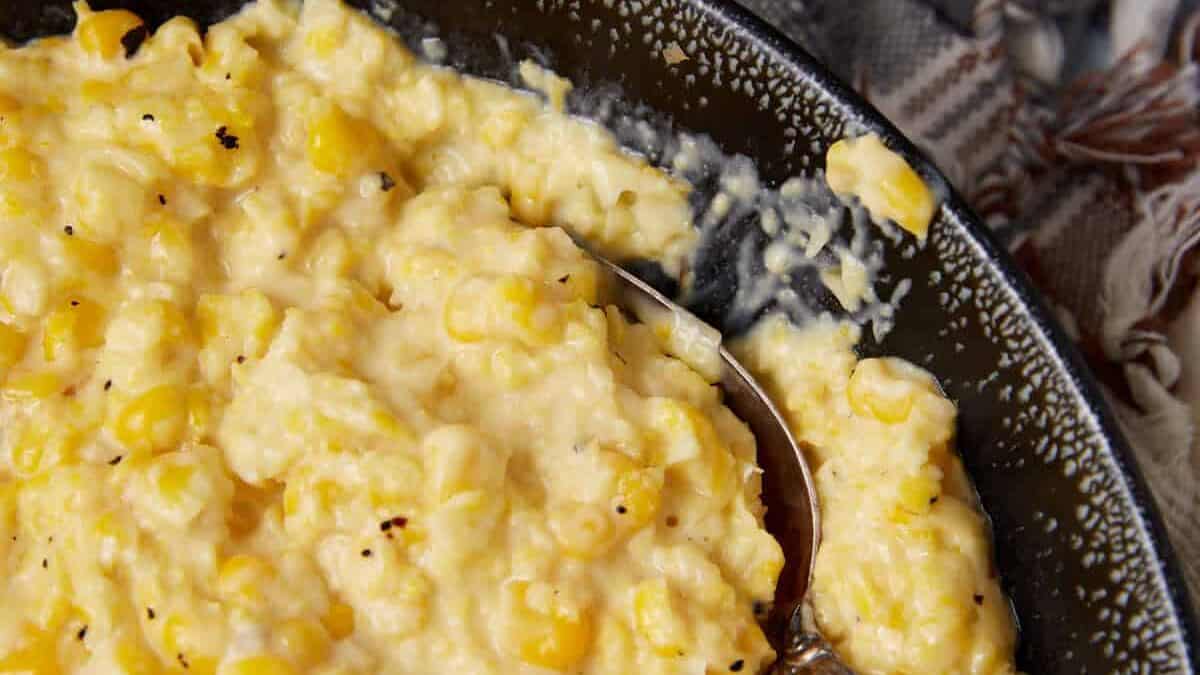 A black bowl filled with creamy, pepper-topped corn sits on a folded beige cloth