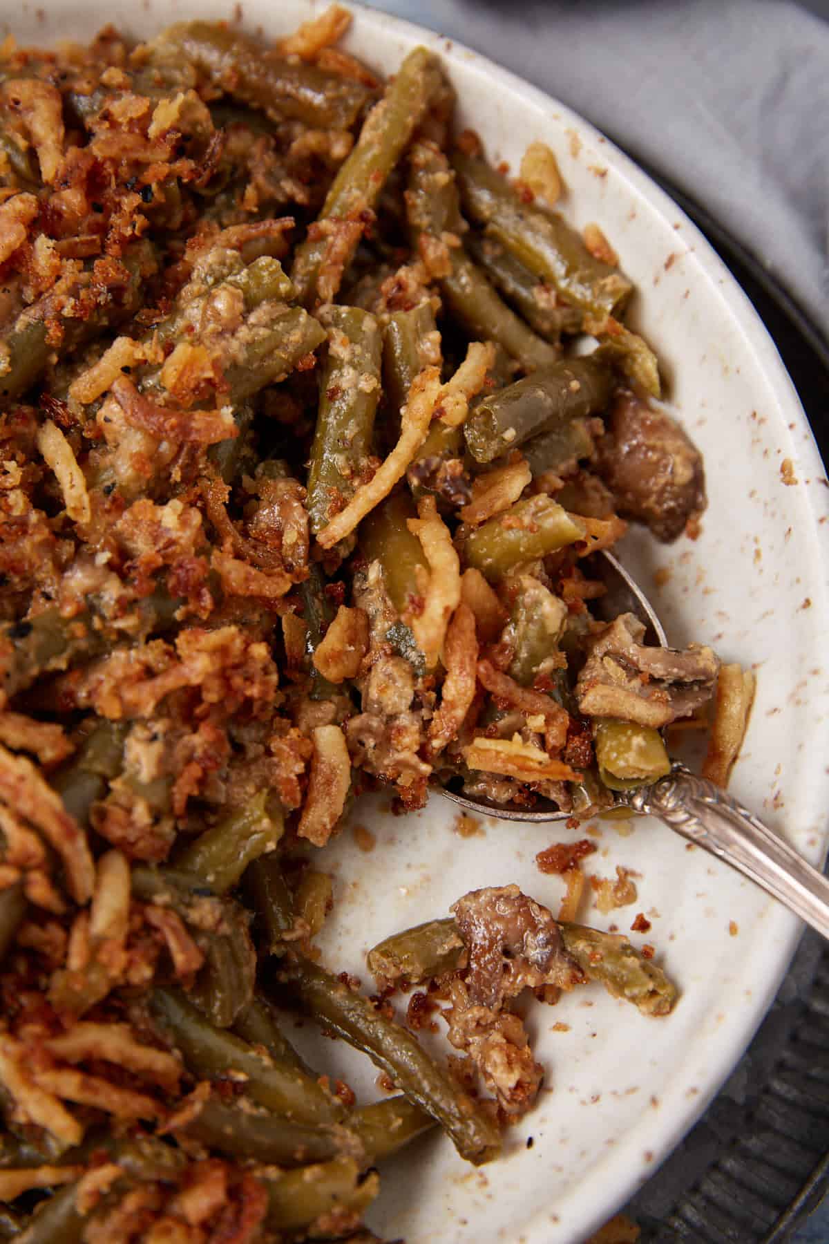 A close-up of a plate of green bean casserole topped with crispy fried onions and breadcrumbs, with a spoon ready to serve.