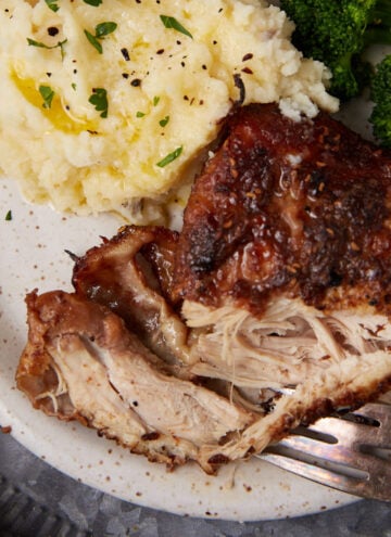 A plate with a serving of shredded roasted chicken, mashed potatoes topped with herbs and butter, and steamed broccoli, with a fork resting on the plate.
