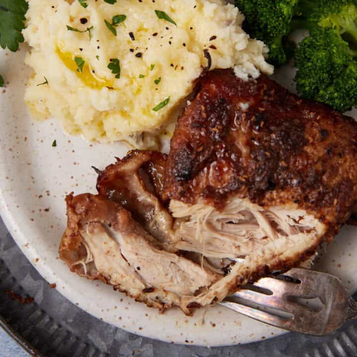A plate with a serving of shredded roasted chicken, mashed potatoes topped with herbs and butter, and steamed broccoli, with a fork resting on the plate.