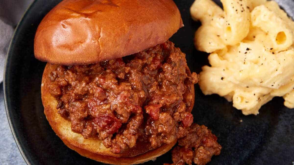 A sloppy joe sandwich with ground beef filling sits on a dark plate 