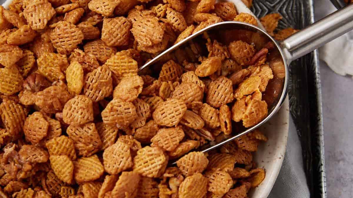 A close-up of a bowl filled with crunchy, golden-brown cereal pieces, with a metal scoop resting on top—just like when I tried these Easter appetizers for a party and served them in creative, festive bowls.
