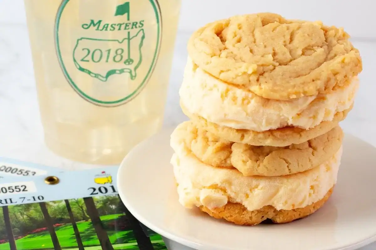 A stack of two ice cream sandwiches made with cookies sits on a white plate. Behind them is a cup with the Masters 2018 logo and a Masters tournament ticket—because your Masters party menu isn't complete without these southern dishes.