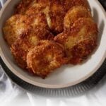 A plate of golden-brown Fried Green Tomatoes with a crispy cornmeal crust sits on a gray cloth. Text at the bottom reads, "Buttermilk Fried Green Tomatoes with the crispiest cornmeal crust.