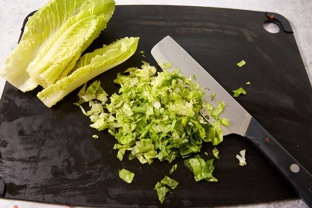 Chopped romaine lettuce and a knife on a black cutting board, with a few whole romaine leaves in the corner.