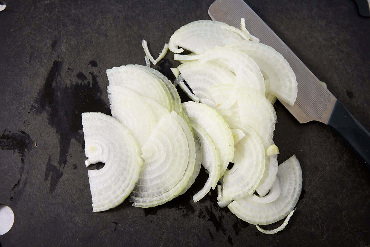 Thinly sliced white onion pieces arranged on a dark cutting board, with a knife nearby—perfect for topping savory French dip sliders.