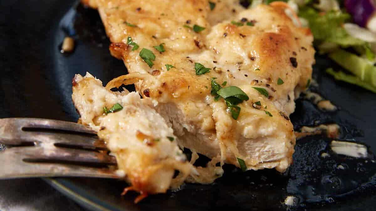 A baked dish of golden, cheesy chicken reminiscent of French dip sliders, topped with fresh chopped 