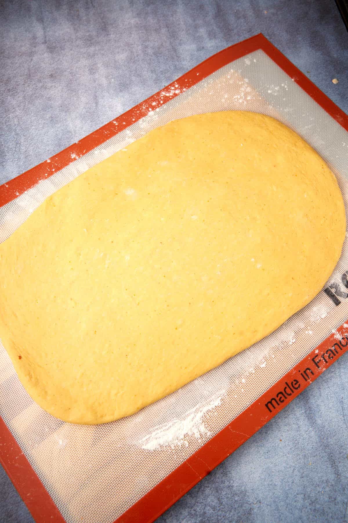 A rectangular sheet of dough rests on a floured silicone baking mat atop a blue countertop.