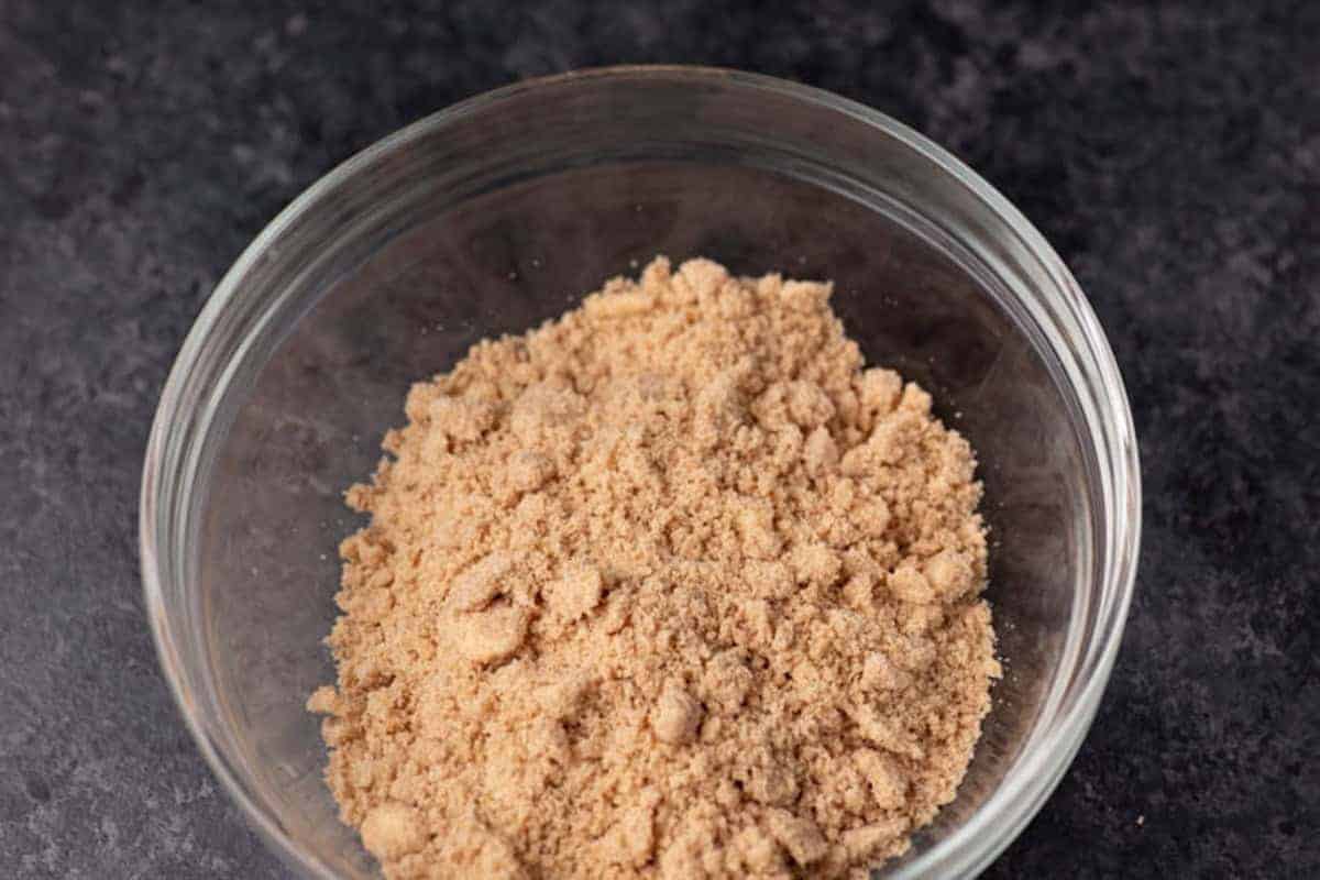 A clear glass bowl filled with light brown, finely ground powder sits on a dark, textured surface.