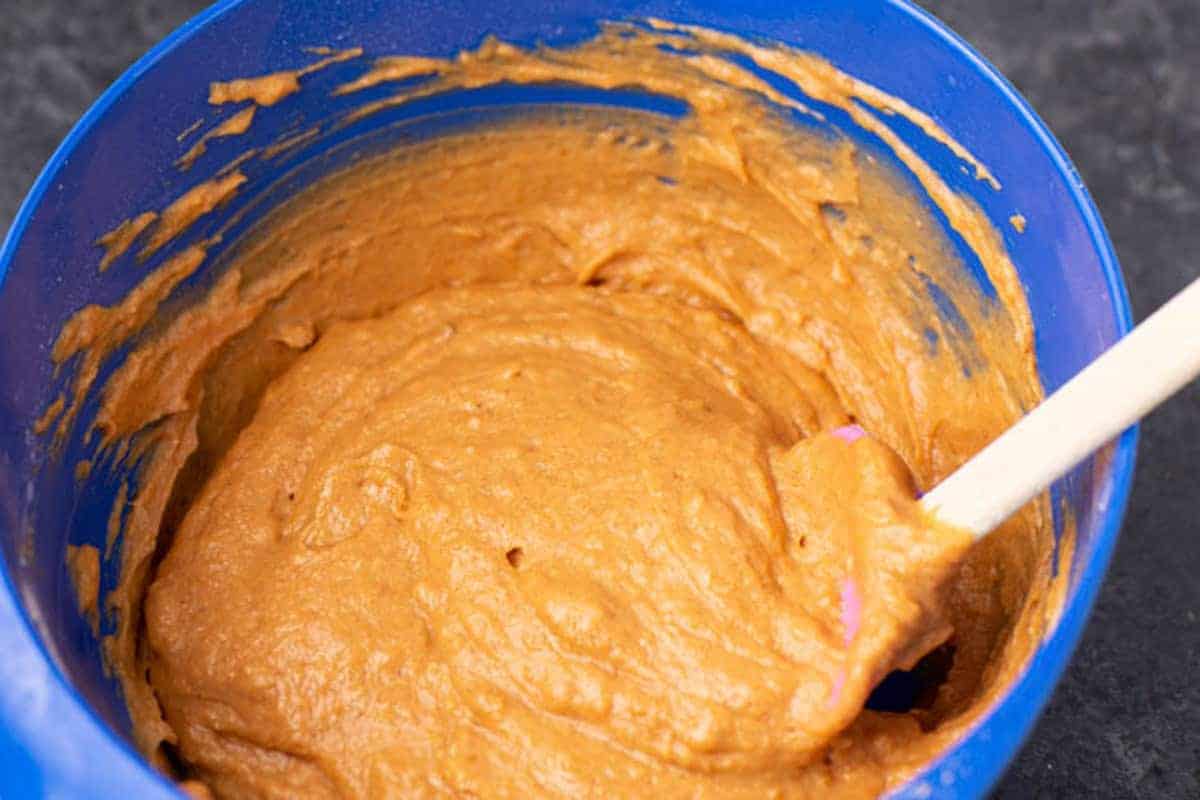 A blue bowl filled with thick orange-brown batter being mixed with a spatula.