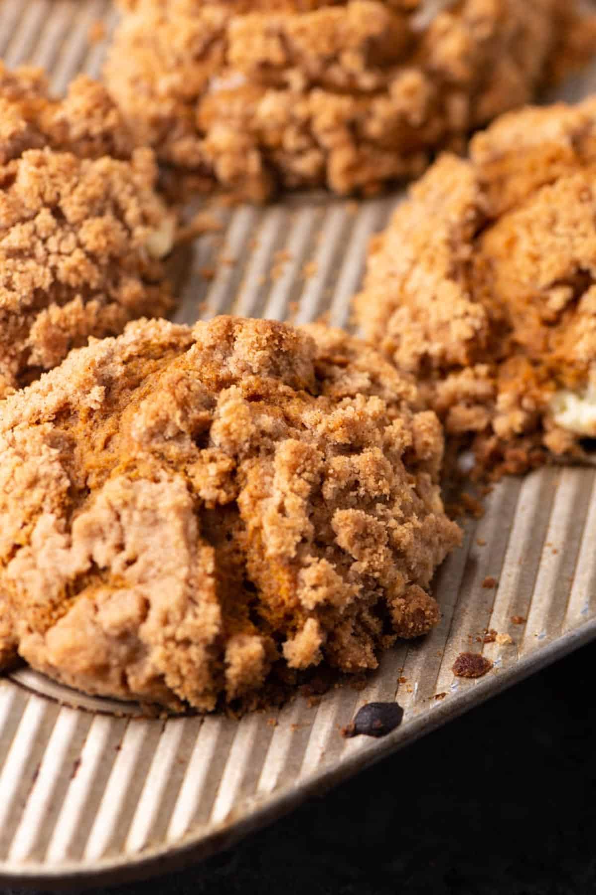 Close-up of golden-brown crumb-topped muffins on a metal baking tray, showing a crispy, textured streusel topping.