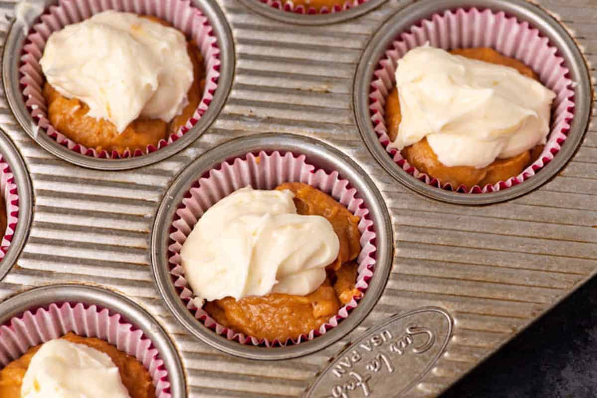 Muffin tin with cupcake liners holds baked cupcakes topped with swirls of creamy white frosting.