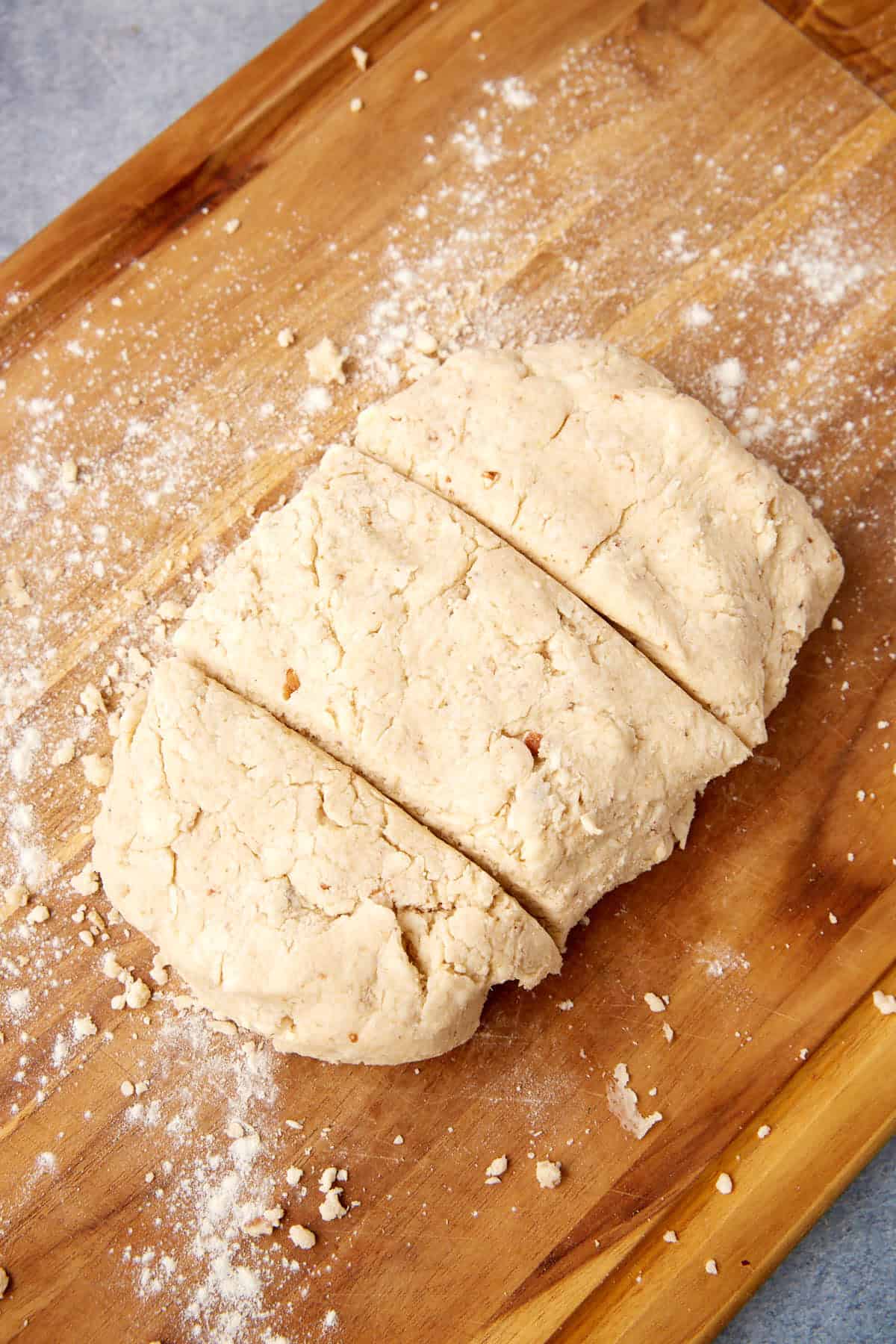 A slab of raw biscuit dough is divided into three sections on a floured wooden surface.