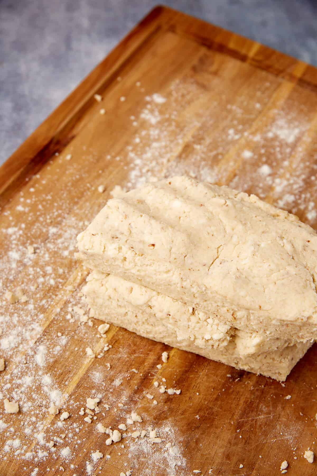 A slab of raw biscuit dough sits on a floured wooden surface, ready to be rolled or cut.