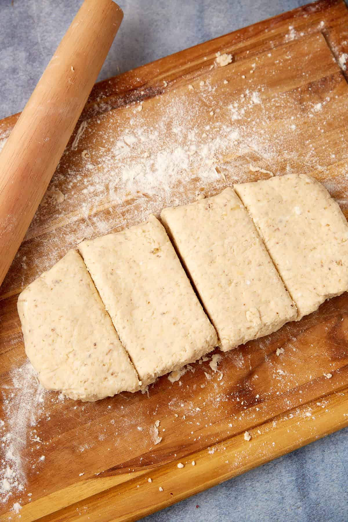 Rectangular block of dough cut into four pieces on a floured wooden board, with a rolling pin nearby.